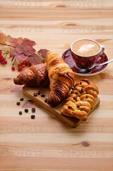 Puff pastry raisin bun and crispy croissant on wooden table with coffee