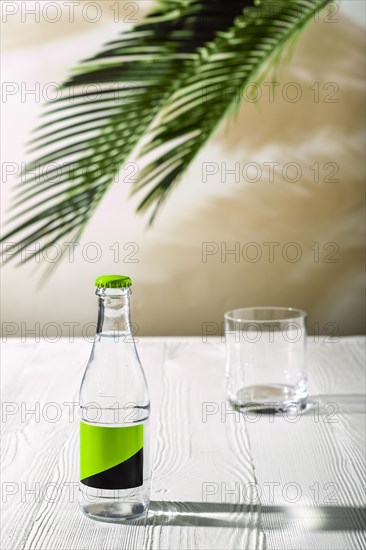 Empty glass on the table and small bottle of tonic water on background under morning sunlight