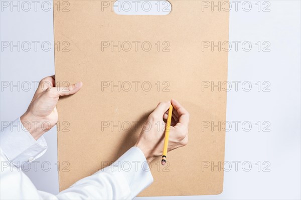 Close up of doctor hands with pencil over clipboard with copy space. Doctor hands writing on blank wooden clipboard isolated. Concept of hands writing on blank wooden clipboard