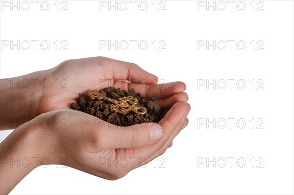 Golden key in handful soil in hand on an isolated background