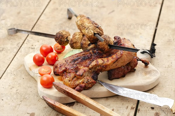 Grilled ribs and champignon on skewer served with fresh cucumber and tomato on wooden table outdoor