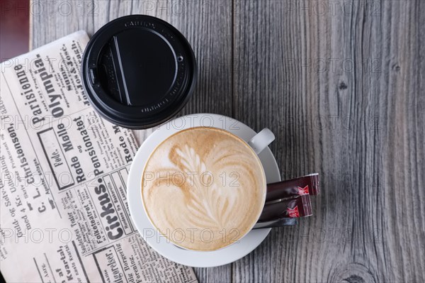 Ceramic and cardboard cup of coffee on wooden table near newspaper. Top view