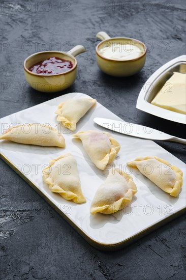 Frozen cherry vareniki on marble serving board with ingredients