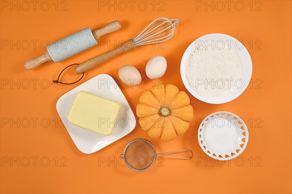 Pumpkin pie ingredients and baking tools on orange background