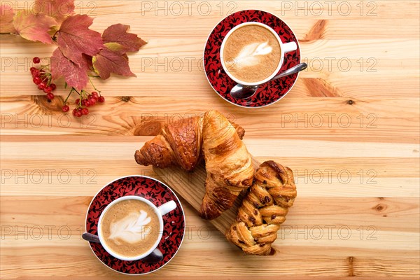 Puff pastry raisin bun and crispy croissant on wooden table with coffee