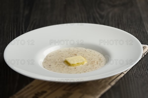 Plate of liquid oatmeal with melting piece of butter on wooden table