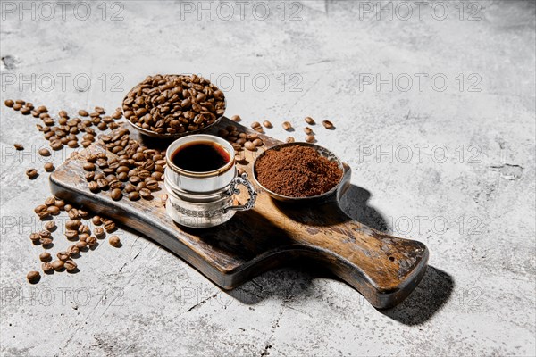 Hot cup of espresso with coffee beans scattered on wooden board and a pot under hard morning sun