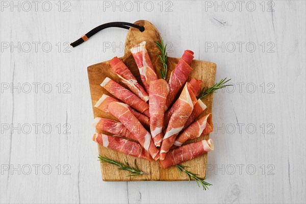 Overhead view of rolled slices of jamon on wooden cutting board
