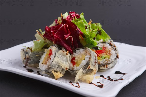 Close up photo of spring rolls in omelet with fresh salad and spicy caramel sauce