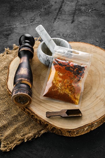 Wooden cross section with a set of spices for pilaf in plastic package and stone mortar and mill