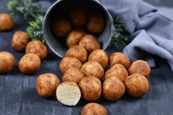 Traditional German Christmas sweets called Marzipankartoffeln. Round ball shaped almond paste pieces covered in cinnamon and cocoa powder spilling out of iron cup on dark background