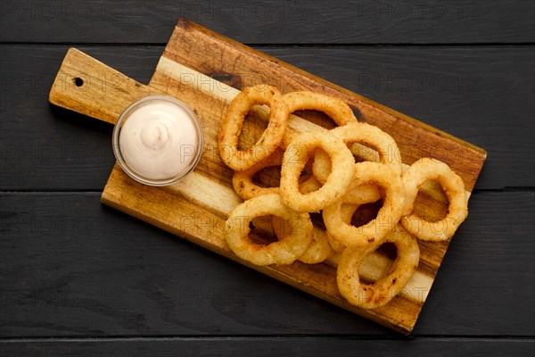 Top view of deep fried breaded squid rings with creamy sauce on wooden serving board
