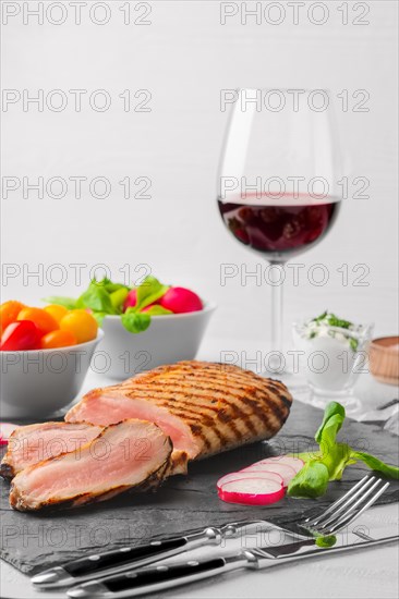 Grilled beef steak medium rare on stone board with fresh vegetables and glass of red wine. Photo with shallow depth of field