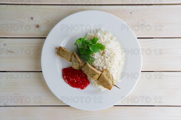 Top view of plate with pork shaslyk with rice and tomato sauce on wooden table