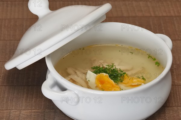 Chicken bouillon in the white bowl on the rustic wooden background. Clear broth in a bowl