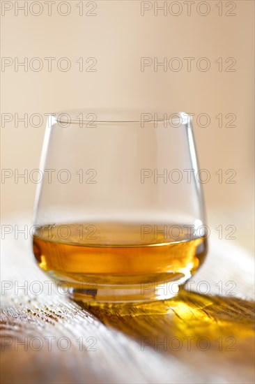 Sniffer glass with whiskey on wooden table in sunlight with hadsh shadow