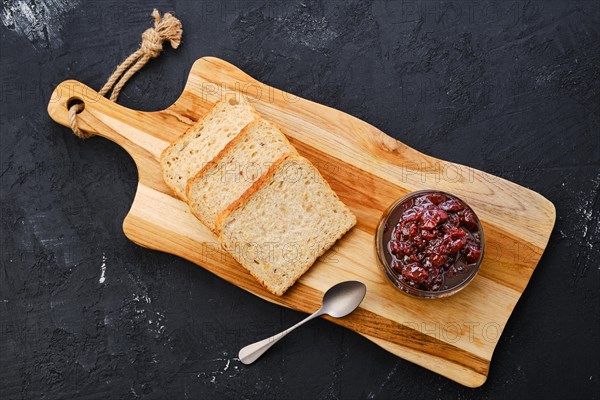 Top view of transparent pot with cherry jam and toast bread