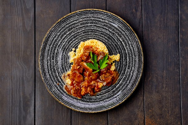 Beef goulash with millet porridge and creamy sauce on dark wooden table