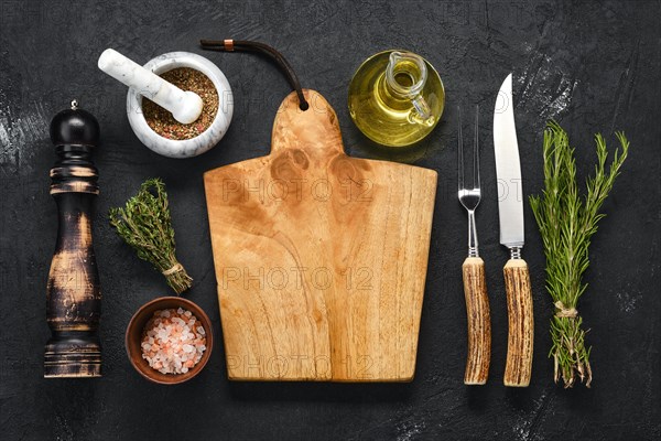 Overhead view of empty wooden cutting board with spice for steak and knife and fork with horn handle