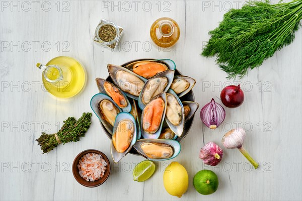 Plate with raw large mussels in half shell with spice on wooden table