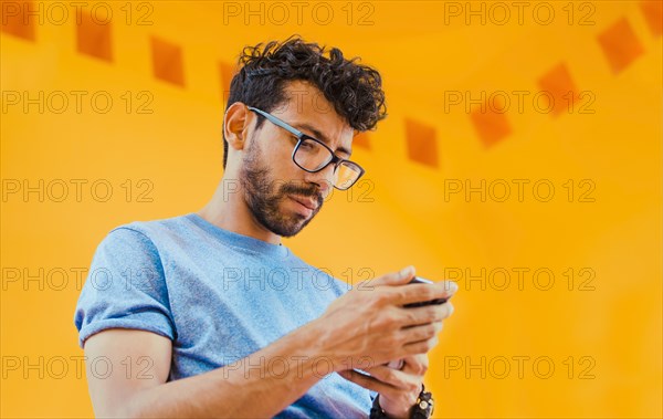 Lifestyle of handsome bearded man using cell phone outdoors. Low angle view of young man using cell phone outdoors. Guy sending a message with a cell phone near a yellow wall outdoors