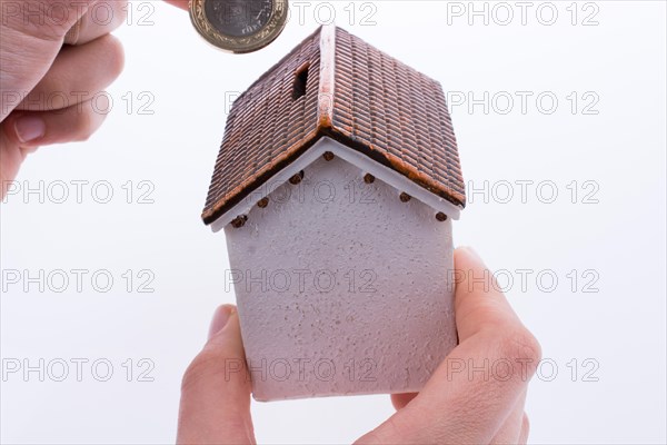 Hand dropping coin into the moneybox in the shape of a model house