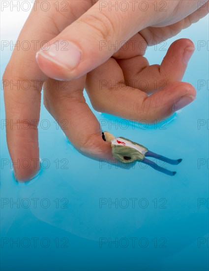 Hand holding a man figurines in water by the side of a Little model house