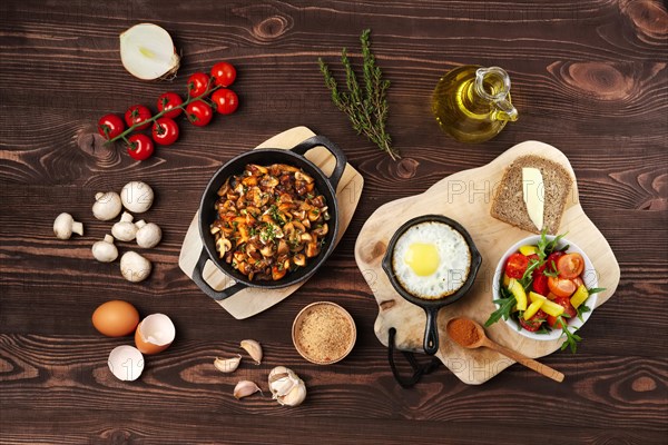 Vegetarian food. Fried mushrooms and egg in cast iron pan. Ingredients for rustic breakfast on wooden table