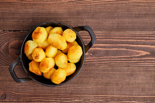 Top view of baked potato in cast iron skillet on natural wooden background