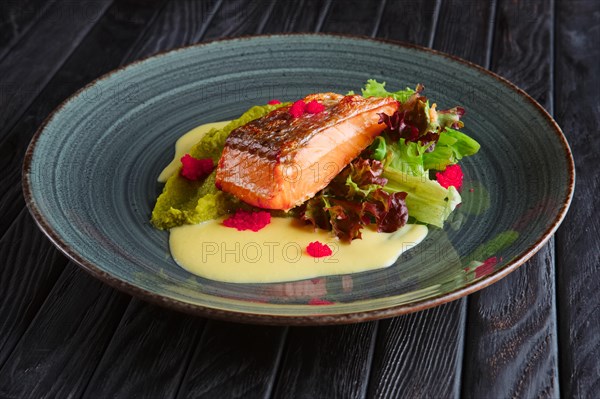 Fried salmon fillet with salad leaves and cream sauce decorated with caviar