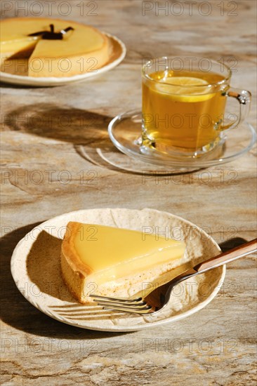 Piece of lemon tart with tea under direct sunlight with hard shadows on the table