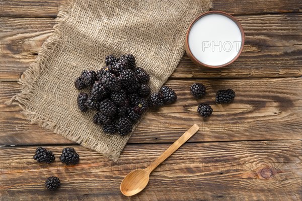 Heap of fresh dewberry on sackcloth table-napkin and clay cup with milk on wooden table