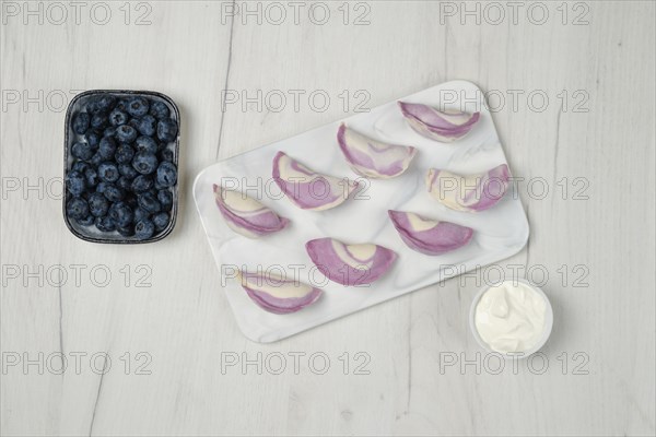 Top view of frozen pierogi with blueberry and sour cream