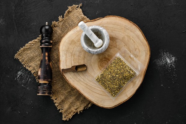 Wooden cross section with lemon pepper in plastic package and stone mortar and mill