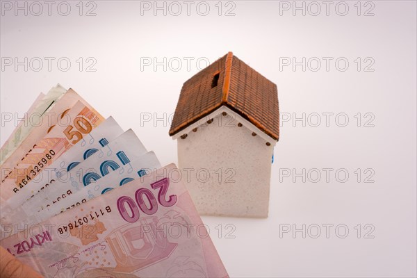 Turkish Lira banknotes by the side of a model house on white background