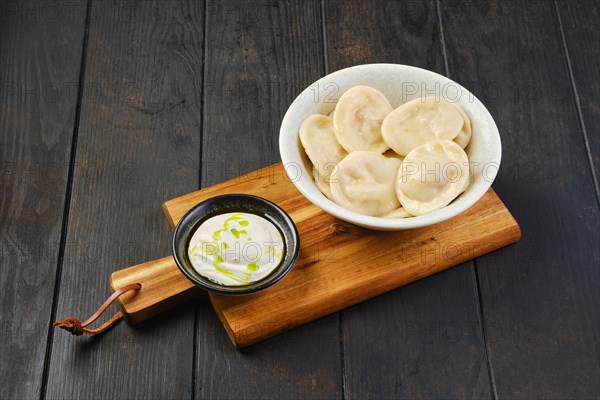 Bowl of pelmeni with curd with sour cream on a wooden serving board