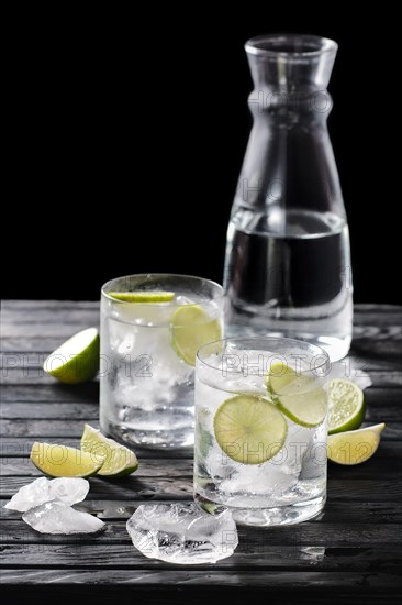 Selective focus composition with gin and tonic cocktail served with citrus on wooden table with pieces of ice