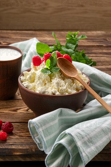 Cottage cheese with wooden spoon on it and milk in clayware on wooden table