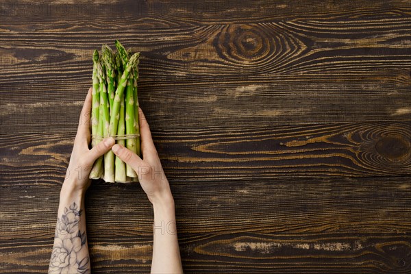 Overhead view of fresh asparagus in hand over wooden background