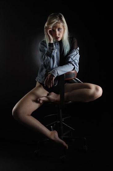 Young blonde woman with jeans jacket sits on chair