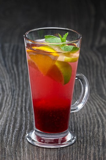 Tall transparent glass with raspberry and citrus tea on dark wooden table