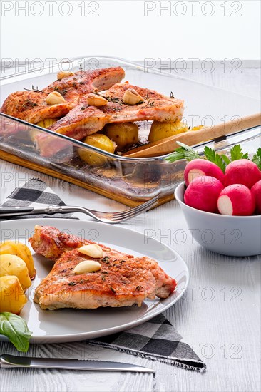 Steak with bone and potato baked in oven in a roasting pan with garlic and thyme