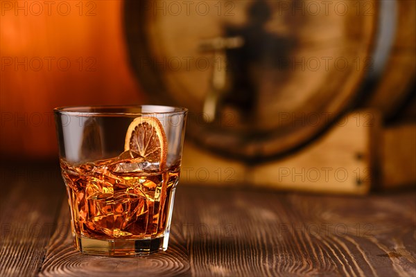 Glass of cocktail with whisky and orange liquor with barrel on background