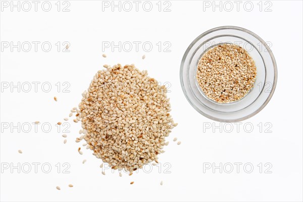 Top view of sesame seeds in a little dish and spilled on white background