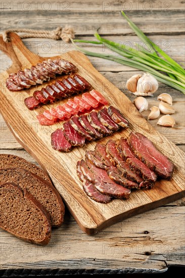 Slices of smoked dried beef and pork meat on wooden cutting board