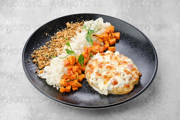 Chopped pork cutlet baked with ham and cheese served with carrot and rice on a plate