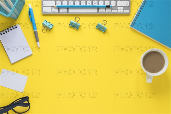 Overhead view keyboard eyeglasses tea cup yellow workspace