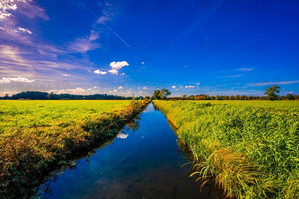 A small irrigation canal between two fields with reflection of clouds and the blue sky in autumn