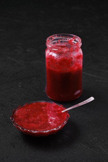 Jar and saucer with cherry jam on black background