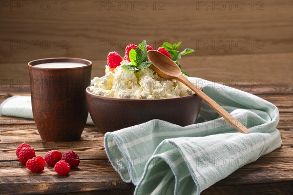 Cottage cheese with wooden spoon on it and milk in clayware on wooden table